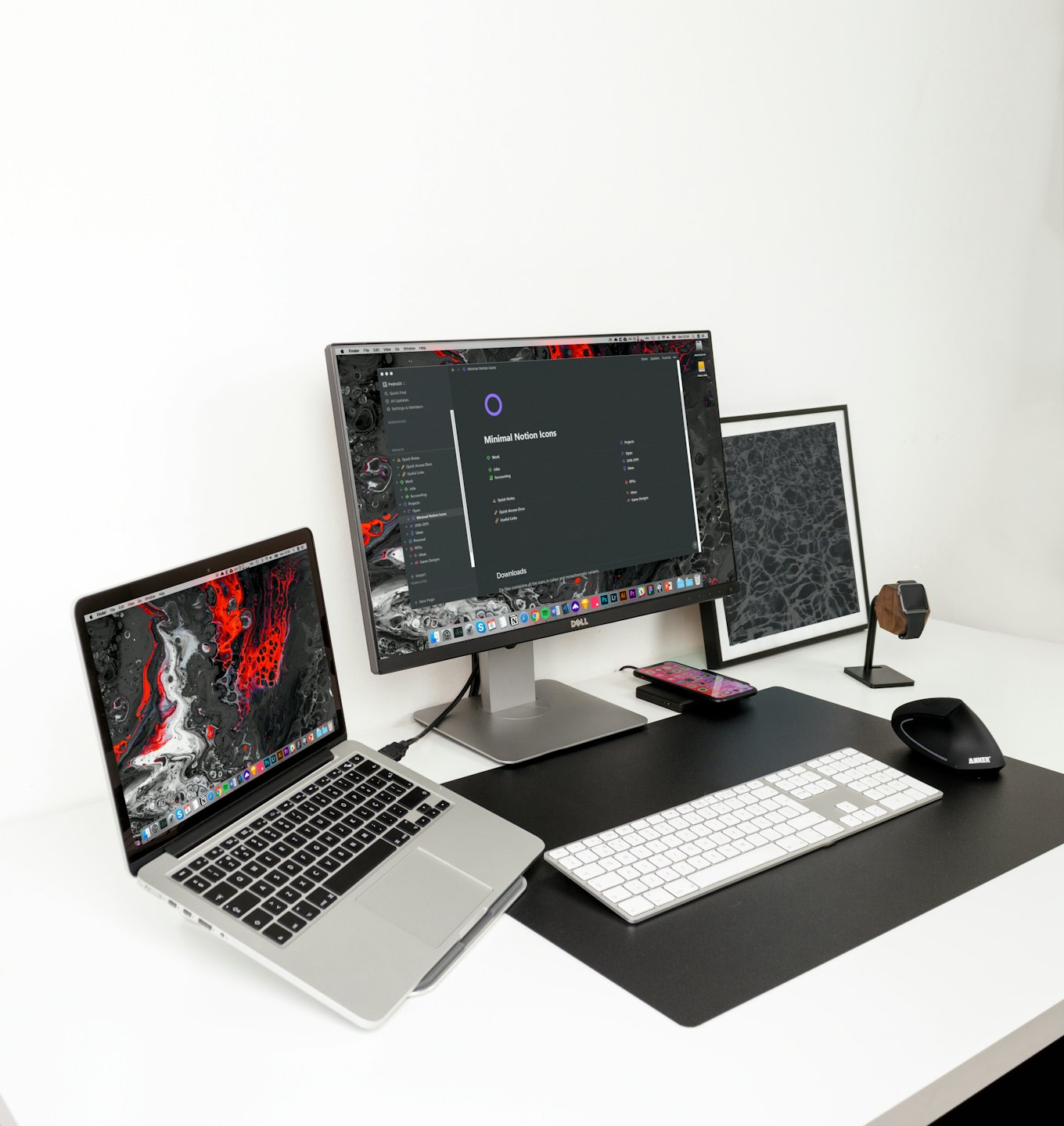 Minimalistický pracovný priestor s notebookom, monitorom a doplnkami na bielom stole.